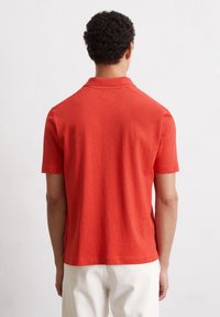 Korte mouwen polo in felrood katoen, met een klassieke kraag, een soepele textuur en lichte zijsplitten aan de zoom.