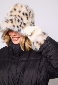 Kapelusz z futra syntetycznego w brązowo-czarny wzór w panterkę, czarna kurtka puchowa i kremowe dziane rękawiczki, z futrzanymi akcentami na mankietach.