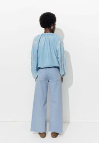 Chemise en denim bleu clair avec des détails brodés, associée à un jean bleu clair à jambes larges. Le modèle porte des chaussures à imprimé léopard.