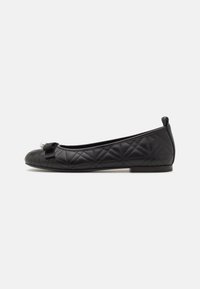 Ballerines noires matelassées avec un bout rond, ornées d'un petit nœud et d'un accent en perles. Matière lisse avec une semelle basse et plate.