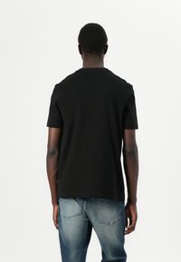 T-shirt nera in cotone con colletto rotondo e maniche corte, caratterizzata da una texture liscia e una vestibilità rilassata, vista da dietro.