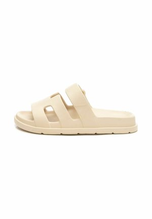 Chanclas beige sin cierre con dos correas anchas y cortes, hechas de un material suave, con una suela texturizada para mayor agarre.