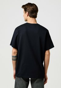 Mustan puuvillan t-paita, jossa on pyöreä pääntie, lyhyet hihat ja rento malli. Suuri tekstuuri; ei näkyviä kuvioita tai yksityiskohtia.