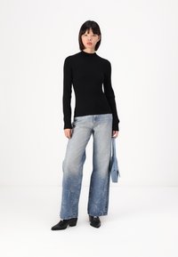 Haut noir à manches longues à côtes, associé à un jean large bleu clair avec un motif d'éclatement, complété par des bottes noires à bout pointu et un sac bleu.
