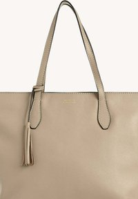 Sac fourre-tout en cuir beige avec deux poignées, doté d'un accent en frange et de détails de couture subtils. Texture lisse avec une marquage doré.