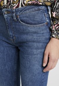 Denim jeans in middelblauw met een lichte vervaging, voorzien van een klassieke vijfzakkenontwerp en zichtbare stikseldetails. Compleet met een knoopsluiting.