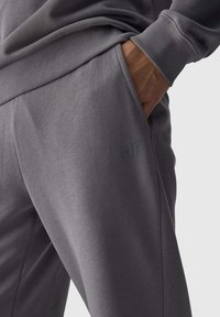 Graue Sweatpants aus weichem Material, mit einer Seitentasche und einem dezenten geprägten Logo am Oberschenkel, in schmal zulaufendem Design.