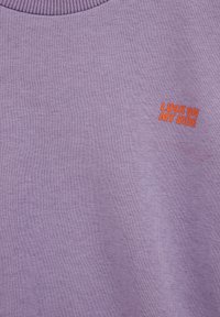 Lila Sweatshirt aus weichem, gestricktem Stoff. Verfügt über einen gerippten Halsausschnitt und orangefarbener, gestickter Text "LUCK ON MY SIDE" auf der Vorderseite.