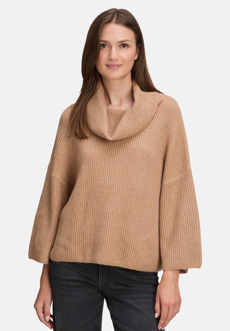 Beige geribbelde gebreide trui met een colhalslijn en wijde mouwen, gemaakt van een zachte stof, gecombineerd met donkere spijkerbroek.