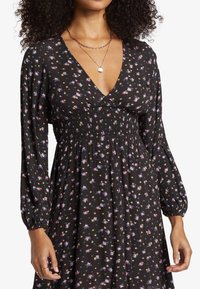 Black floral dress featuring long, puffed sleeves, a deep V-neckline, smocked waist, and a flowing skirt adorned with multicolored floral patterns.