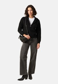 Czarny rozpinany sweter z kapturem i sznurkiem, w połączeniu z szarymi spodniami dzwonowymi i czarnymi botkami na obcasie. Mała torba na ramię.