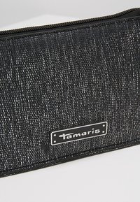 Svart texturerad plånbok med en glänsande finish, med en framträdande varumärkeslogotyp i en rektangulär silverfärg. Dragkedjestängning längst upp.