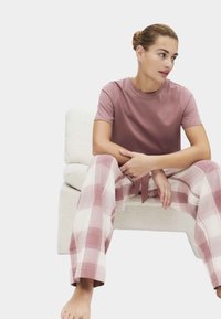 Rosa bomullst-shirt kombinerad med rutiga loungebyxor i ljusrosa och kräm. Byxorna har dragsko och vida ben. Sitter på en vit stol.