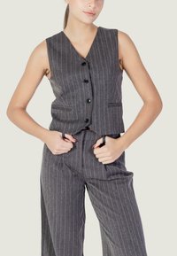 Gilet grigio a righe sottili con scollo a V, caratterizzato da sei bottoni neri e tasche laterali. Il tessuto sembra strutturato, abbinato a pantaloni coordinati.