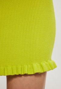 Strickrock in leuchtendem Gelb mit gerippter Textur und einem Rüschensaum. Das Material wirkt weich und dehnbar und sorgt für eine enge Passform.