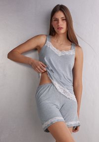 Grijze katoenen slaapset met een mouwloze top met kanten rand en bijpassende shorts. Zachte textuur, ontspannen pasvorm en kanten accenten aan de randen.