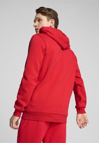 Rød hættebluse lavet af blødt materiale, med ribkant i bunden og ved ærmerne. Bagsidevisningen viser en glat tekstur og minimalistisk design.