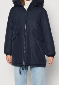 Giacca imbottita navy con cappuccio, chiusura con zip frontale, polsini elastici e due ampie tasche laterali. Presenta un cordino al fondo per le regolazioni.