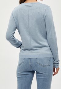 Ljusblå stickad tröja med långa ärmar, ribbade muddar och en mönstrad backseamsdetalj, ihop med ljusblå denimjeans.