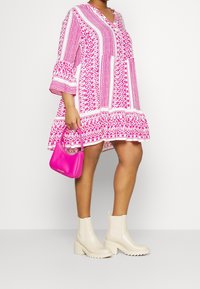 Vestido rosa con estampado, mangas abullonadas, con un largo hasta la rodilla, acompañado de un pequeño bolso rosa y botines de tacón ancho beige.