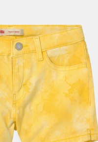 Żółte dżinsowe szorty w wzór tie-dye, z zapięciem na guzik, szlufkami na pasek i kieszeniami z przodu. Gładka tekstura i casualowy design.