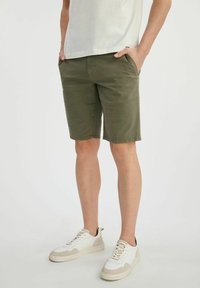 Szorty w kolorze khaki wykonane z mieszanki bawełny, z kieszeniami i prostym krojem, w połączeniu z białymi i beżowymi sportowymi sneakersami.