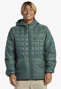 Green, quilted puffer jacket with a hood, featuring a zippered front, chest pocket, and side pockets. Smooth, shiny texture.