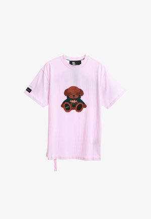 Camiseta de algodón rosa con un oso de peluche marrón bordado en un traje verde. Mangas cortas con una etiqueta en el brazo izquierdo.