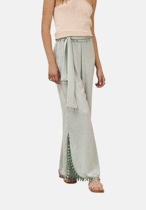 Pantalones de pierna ancha verde claro con aberturas laterales y acentos de borlas; combinados con una blusa durazno de un solo hombro con detalles perforados.