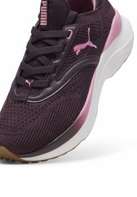 Purpuriniai sportiniai bateliai su tekstūruotu tinkleliu, rožinėmis detalėmis, balta tarpine ir guminiu padu. Yra raišteliai ir PUMA ženklas.