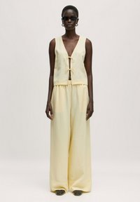 Geel, mouwloos topje met een V-hals en strikdetail, gecombineerd met wijde, vloeiende broek in een bijpassende kleur. Effen textuur, minimaal ontwerp.