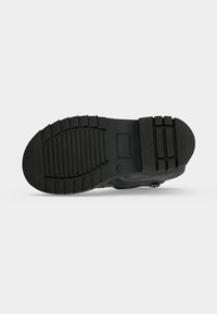 Semelle en caoutchouc noire d'une chaussure avec des motifs de semelle épais incluant des rainures horizontales et des blocs rectangulaires pour l'adhérence et la durabilité.