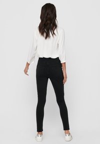Los jeans negros ajustados presentan una cintura alta y un diseño suave y ajustado. Una camiseta blanca de mangas largas complementa el atuendo, combinada con zapatillas plateadas.