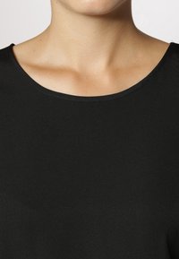 Haut noir à manches courtes avec un col arrondi, fabriqué dans un tissu lisse. Le matériau semble léger et présente un léger éclat.