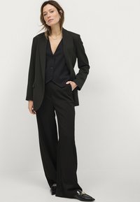 Zwarte gepakte kostuum met een dubbelgegane blazer, brede broek en een fitted gilet. Glad stof met minimalistische ontwerpdetails.