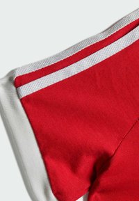 Červená tkanina s bielymi detailmi, ktorá obsahuje textúrovanú pleteninu a hladký golier. Dizajn má kontrastné pruhy pozdĺž okrajov.