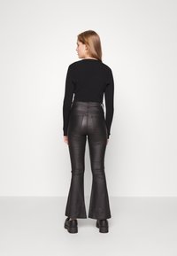 Sweater preto de malha canelada de mangas compridas combinado com calças pretas de cintura alta e boca de sino. Textura suave e costuras definidas; sapatos pretos de plataforma robusta.