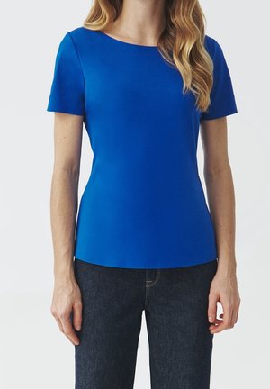 Haut bleu à manches courtes avec un col rond, fabriqué à partir d'un tissu lisse. Coupe ajustée, associé à un jean en denim foncé, mettant en valeur des lignes épurées.