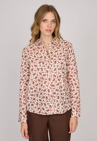 Blouse à manches longues en tissu crème clair, avec un imprimé paisley dans des teintes de brun-roux et des accents blancs, dotée d'une fermeture à boutons sur le devant.