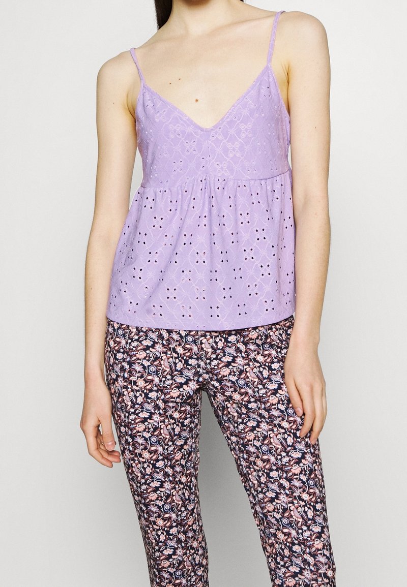 Ljuslila ärmlös topp med hålstickade detaljer, med V-ringning och rynkad midja, tillsammans med byxor med mörkt blommönster.