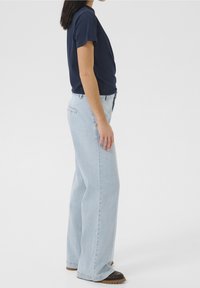 Sinisen puuvillapaitaan yhdistetty vaaleansiniset väljät farkut. Farkuissa on etutaskut, takataskut ja hieman kulunut ilme.