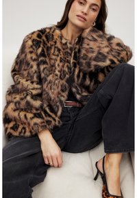 Leopard print faux fur jacket with wide sleeves, soft texture, and black trim, paired with high-waisted dark jeans and strappy heels.