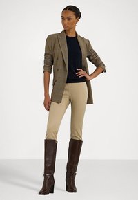 Ruutukuvioinen kaksirivinen bleiseri ruskeana, navy-sinisen yläosan päällä, beige-housujen ja polveen yltäviä ruskeita nahkasaappaita, joissa on korkea korko.