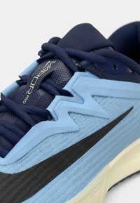 Γαλάζιο αθλητικό παπούτσι με υφή σε μπλε και μαύρο, ναυτέρες κορδόνια και λείο πάτο με εμφανές σχεδιαστικό στοιχείο.