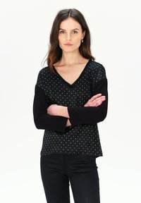 Schwarzes V-Ausschnitt-Oberteil mit langen, einfarbig schwarzen Ärmeln und einem gepunkteten Muster in Hellblau auf dem Körper. Glatter Stoff mit einer lockeren Passform.