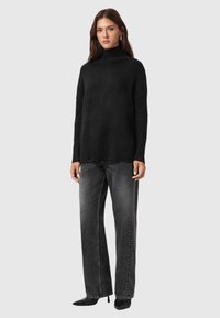 Jersey negro de cuello alto con ribetes en el dobladillo, combinado con jeans rectos de color gris claro y tacones negros de punta. Tela texturizada.