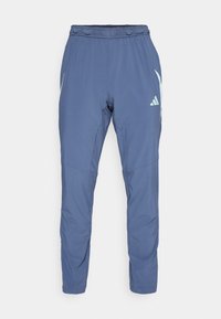 Pantalon de sport bleu marine en tissu léger, avec une taille élastique, une coupe fuselée et un logo de marque blanc sur le côté.