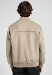 Beige wollen-blend jas met ribbelkraag en -manchetten, met een gestructureerde afwerking en silhouet. De achterkant toont het stiksel-details.