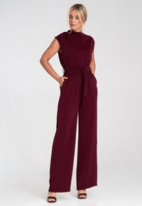 Burgundowy kombinezon z krótkimi rękawami, szerokimi nogawkami i paskiem w talii. Wykonany z gładkiego materiału o prostym designie, z bocznymi kieszeniami.