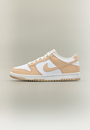 Niski but sportowy Nike z beżowymi nakładkami, białą bazą, beżowym znakiem Swoosh, białymi sznurówkami i beżową podeszwą na neutralnym tle.